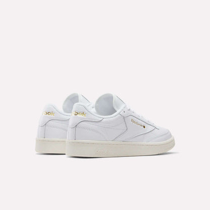 A pair of Reebok Men's Club C 85 Shoes in white garment leather with gold logo accents, white laces, and beige rubber soles—displayed angled to show side and back views against a plain light background.