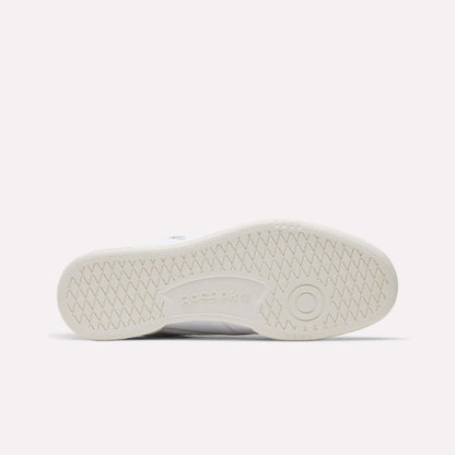 The image shows the sole of a white Reebok Men's Club C 85 Shoe, featuring a herringbone tread pattern and an embossed Reebok logo at the center, highlighting classic retro style.