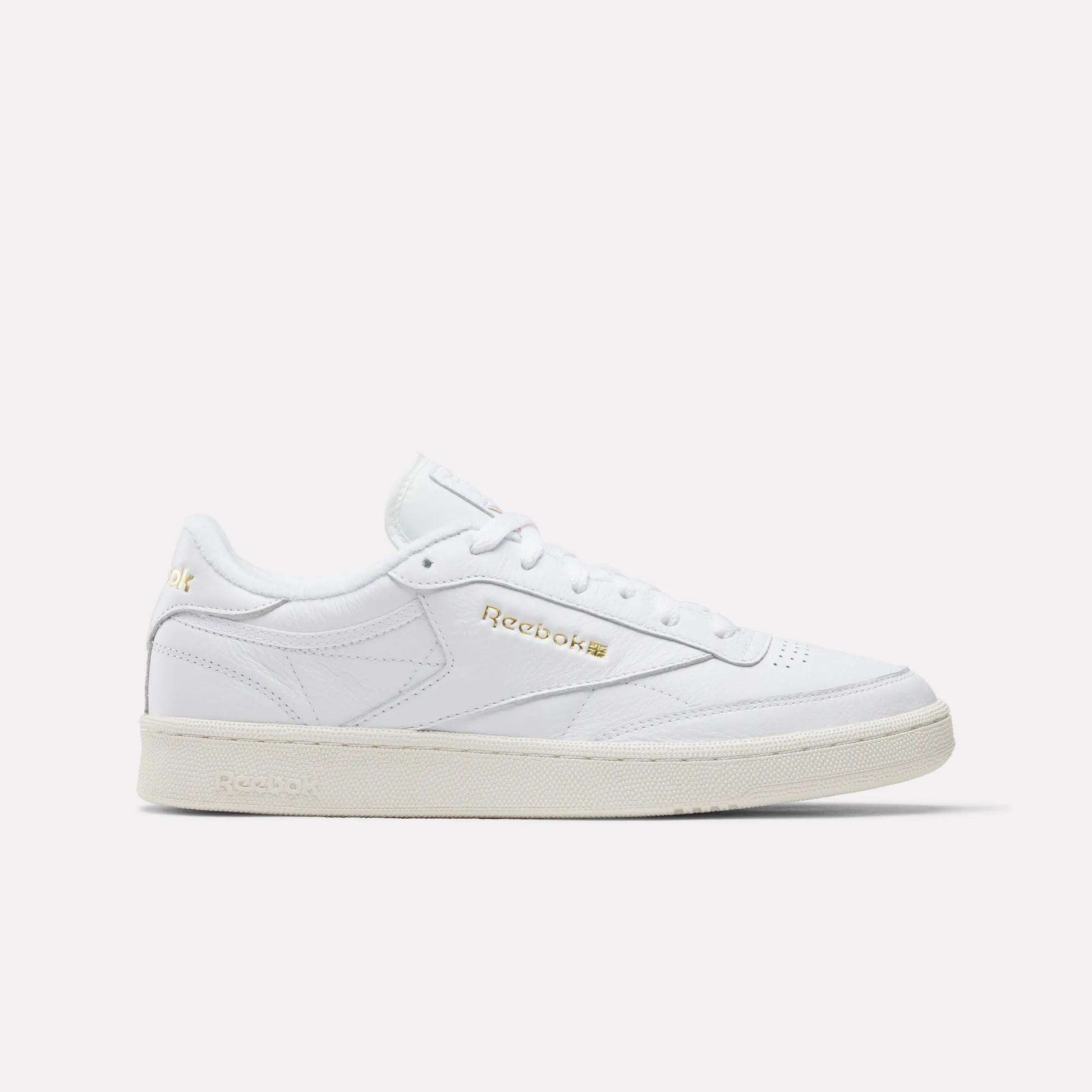 The Reebok Men's Club C 85 Shoes in Ftwr White/Chalk/Gold feature premium leather, a low-top silhouette, gold branding, white laces, and a slightly off-white sole, displayed on a plain white background.