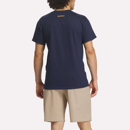A man faces away from the camera wearing a Reebok Men's Crushers Tee in navy and beige shorts against a plain white background.