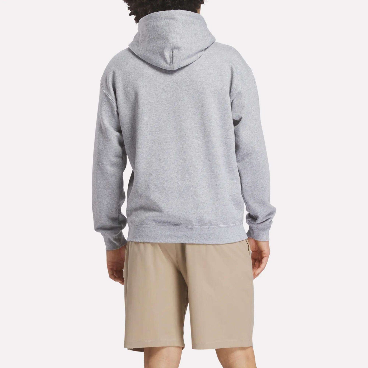 A person faces away from the camera, wearing a light gray Reebok Men's Crushers Hoodie and beige shorts against a plain, light background.