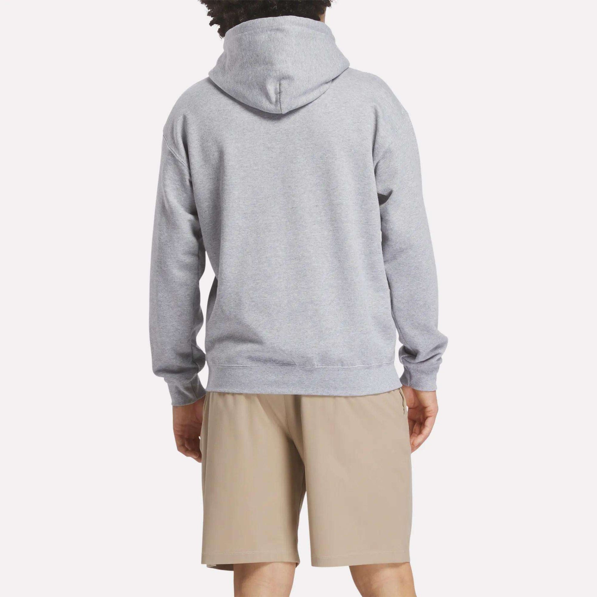 A person faces away from the camera, wearing a light gray Reebok Men's Crushers Hoodie and beige shorts against a plain, light background.