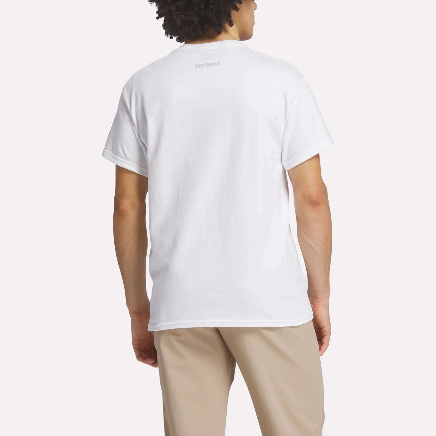 A person is shown from the back, wearing a Men's Crushers Icon Tee by Reebok in plain white and beige pants, standing against a light background.