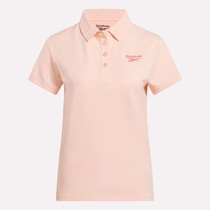 The Reebok Women's Micro Pique Polo Shirt is light pink with stretch fabric, short sleeves, a collar, button placket, and a pink Reebok logo on the left chest. It is displayed against a plain white background.
