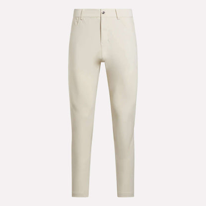 The Reebok Men's Favorite 5-Pocket Relaxed Fit Golf Pants, in light beige wrinkle-resistant fabric with belt loops, button closure, and front pockets, are shown against a plain white background.