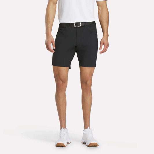 A man models Reebok Men's Favorite Golf Shorts 8.5", paired with a white polo, black belt, and white sneakers against a plain white background; only his body from the shoulders down is shown.