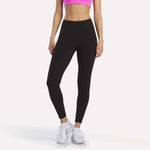 A person models Reebok Women's Odyssey High-Rise 7/8 Leggings and a bright pink sports bra with white athletic shoes, standing against a plain white background. The model’s head is not visible in the image.