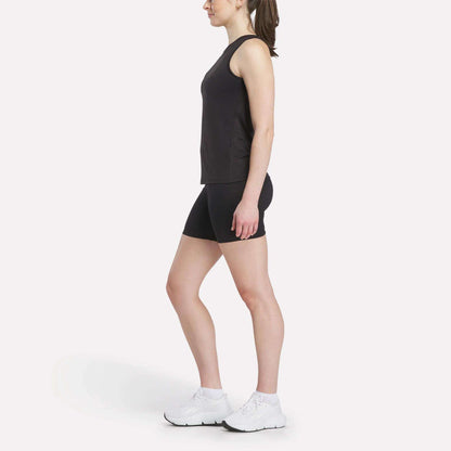 A woman in profile faces left, wearing a Reebok Women's Marled Performance Tank Top and black shorts with white athletic shoes—ideal activewear—set against a plain white background.