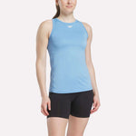 A woman wears a Reebok Women's Marled Performance Tank Top in light blue with black shorts, standing against a plain white background.