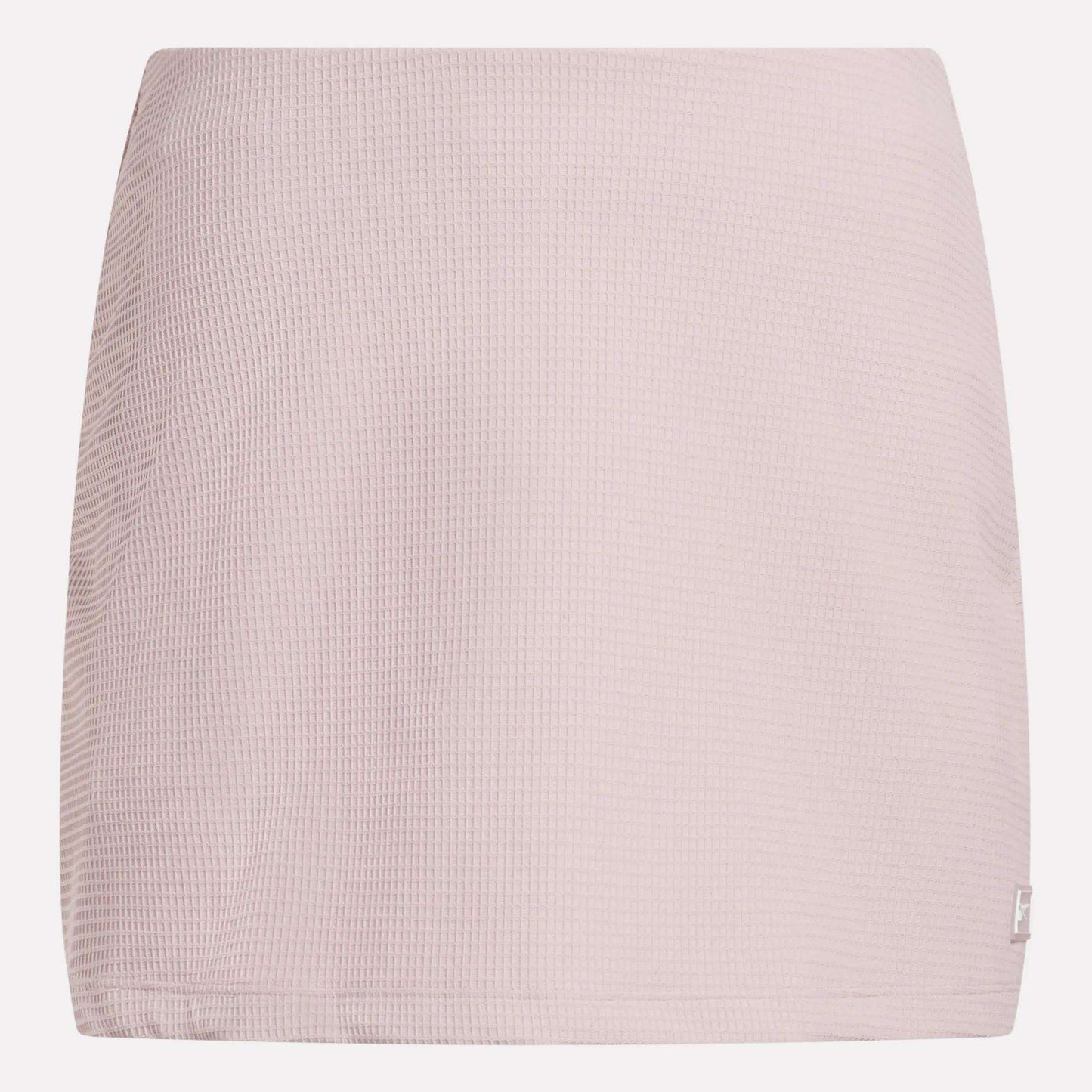 The Reebok Women's Time Out Slim Tennis Skort features a light pink, waffle-textured fabric and straight cut—a minimal design ideal for sporty flair in your activewear wardrobe. Shown against a white background.