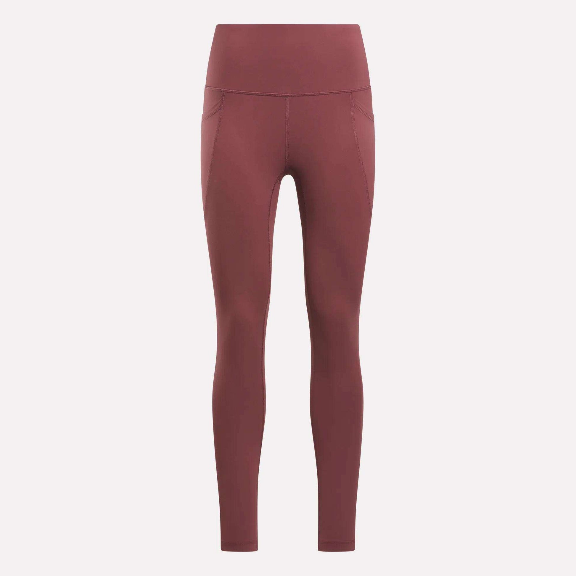 Reebok Women's High-Rise Tights in a muted reddish-brown feature side pockets, visible seam details, and a high-rise waistband. These full-length training tights are displayed on a plain light background.