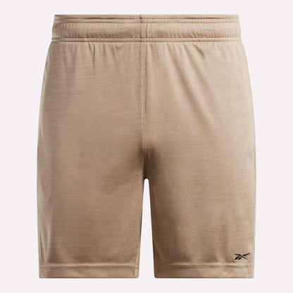 The Reebok Men's Inclination Shorts feature tan, soft fabric and an elastic waistband. A small black Reebok logo accents the lower left leg. These athletic shorts are shown against a plain, light background.