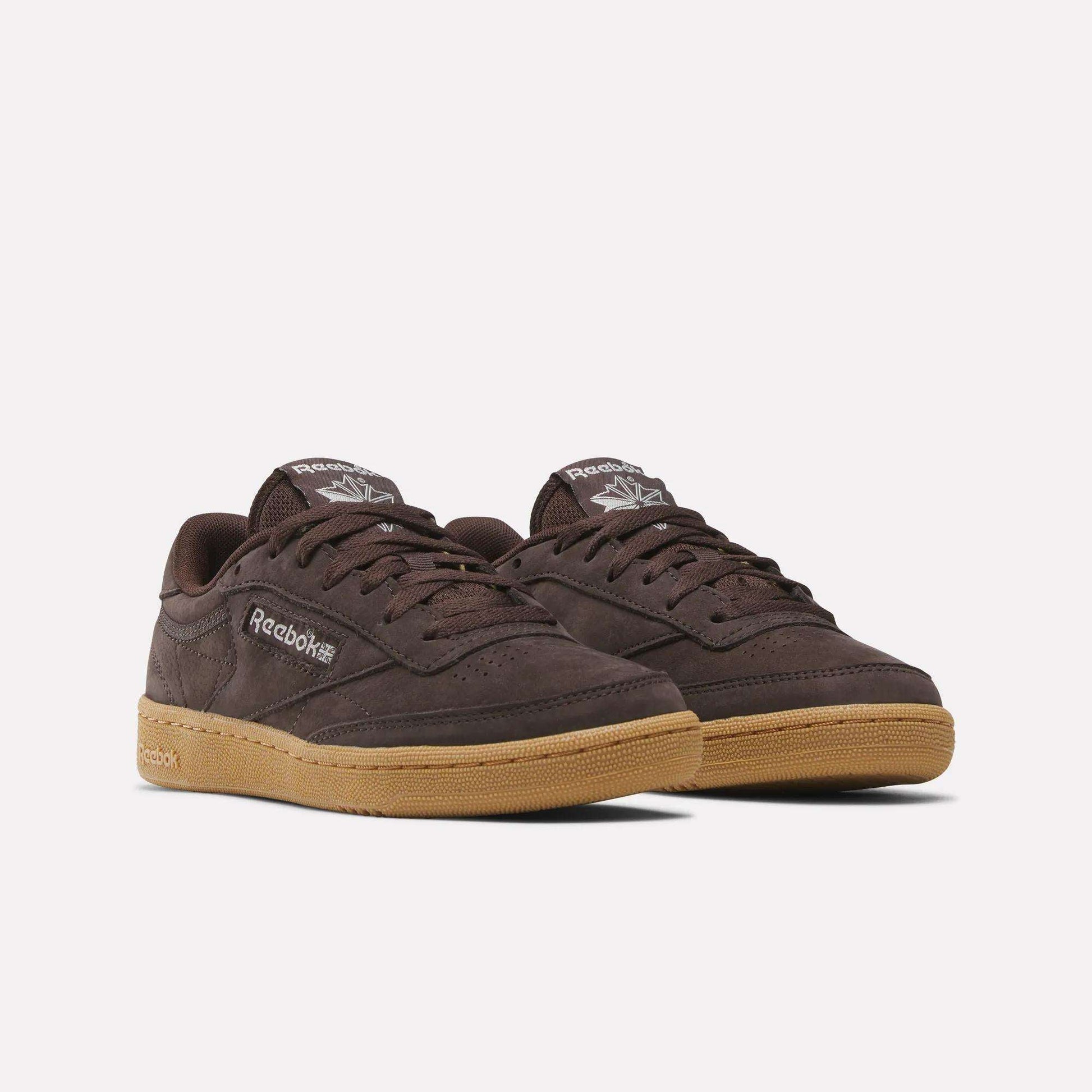 Reebok Women's Club C 85 Shoes in dark brown with gum soles, featuring Reebok logos on the side and tongue, are classic leather sneakers shown on a plain white background—timeless style from Reebok.