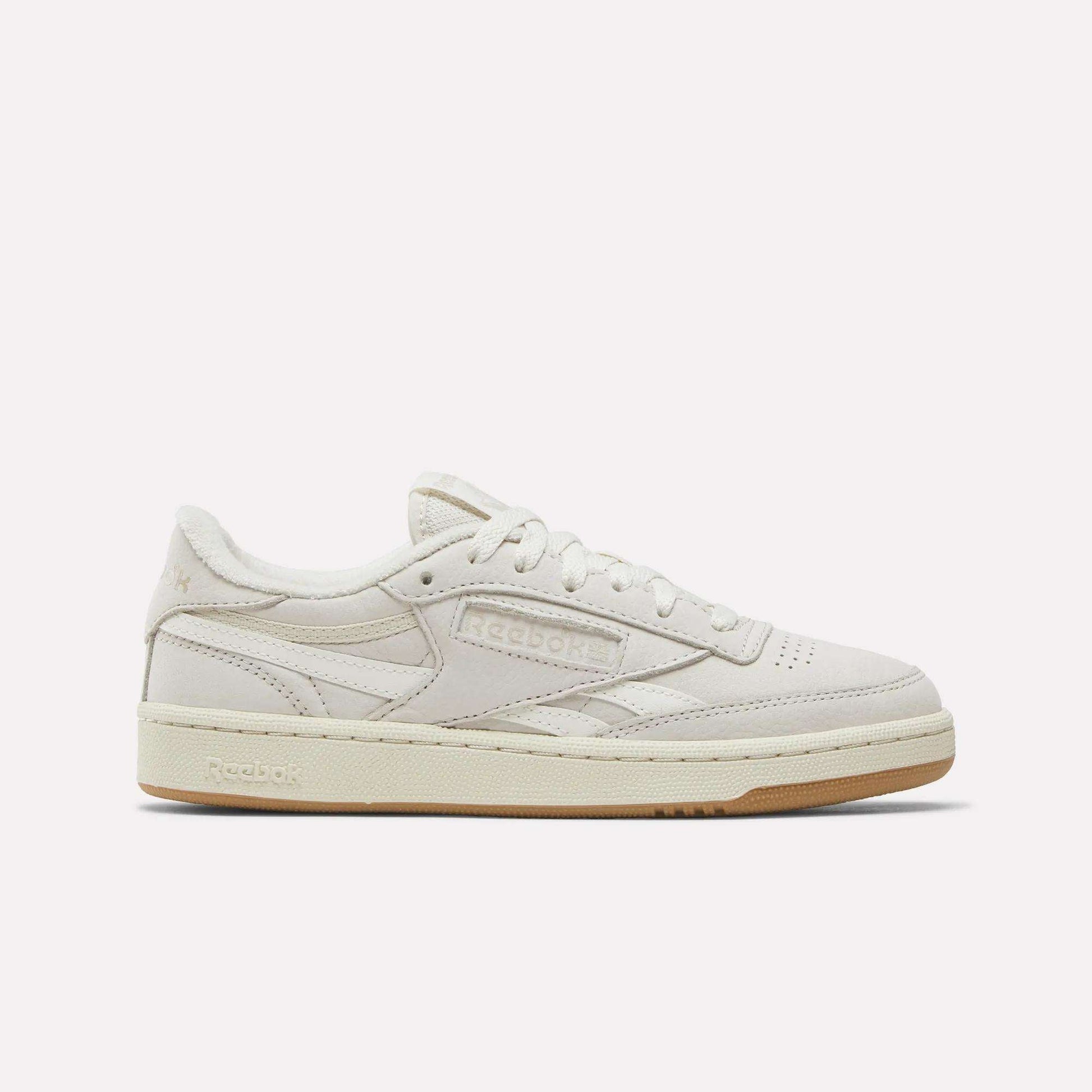 The Reebok Women's Club C Revenge Shoes feature a beige low-top design with a suede and nubuck leather upper, beige laces, and a light brown rubber sole, displayed in side profile on a plain white background.