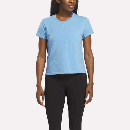A woman wearing a Vector Peri Blue Reebok Women's Graphic Glow Top and black leggings stands facing forward against a plain white background.