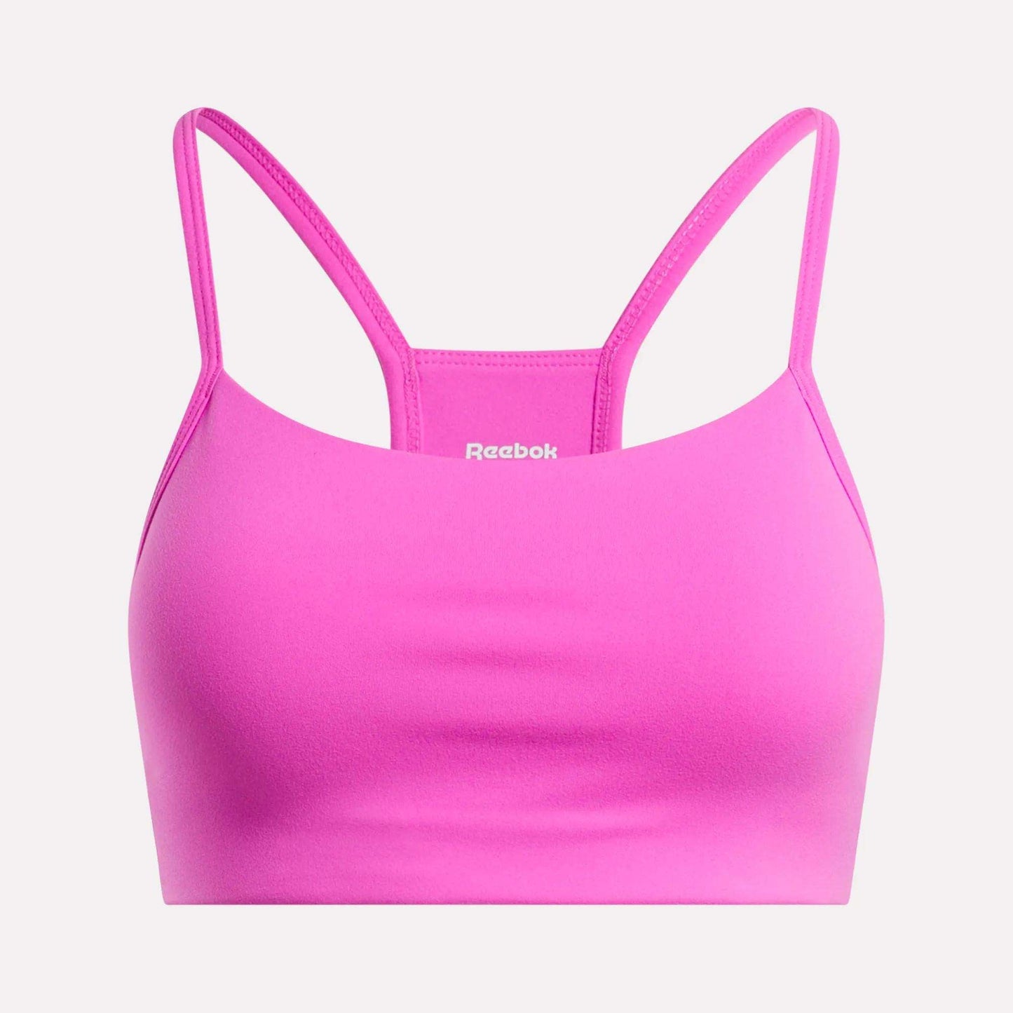 The Reebok Women's Low-Impact Sports Bra is bright pink with thin adjustable straps and a smooth, simple design. The white Reebok logo appears on the front center. Ideal for light-impact training.