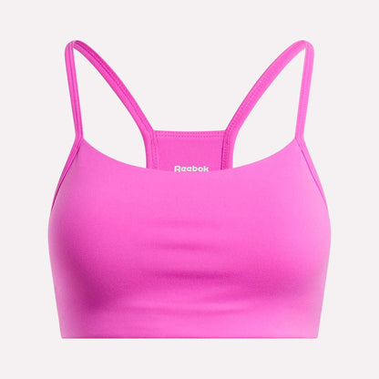 The Reebok Women's Low-Impact Sports Bra is bright pink with thin adjustable straps and a smooth, simple design. The white Reebok logo appears on the front center. Ideal for light-impact training.