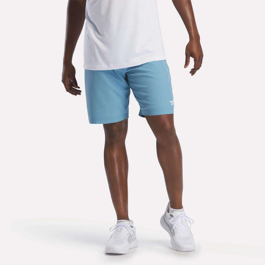 A person wearing a white shirt, Reebok Men's Range Shorts 9" in Warped Blue, and white sneakers stands against a plain white background.