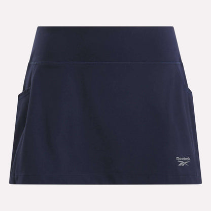 The Women's Break Point Skort by Reebok is a navy blue training skort featuring side pockets, built-in compression shorts, and a small logo on the lower right, shown against a light background.
