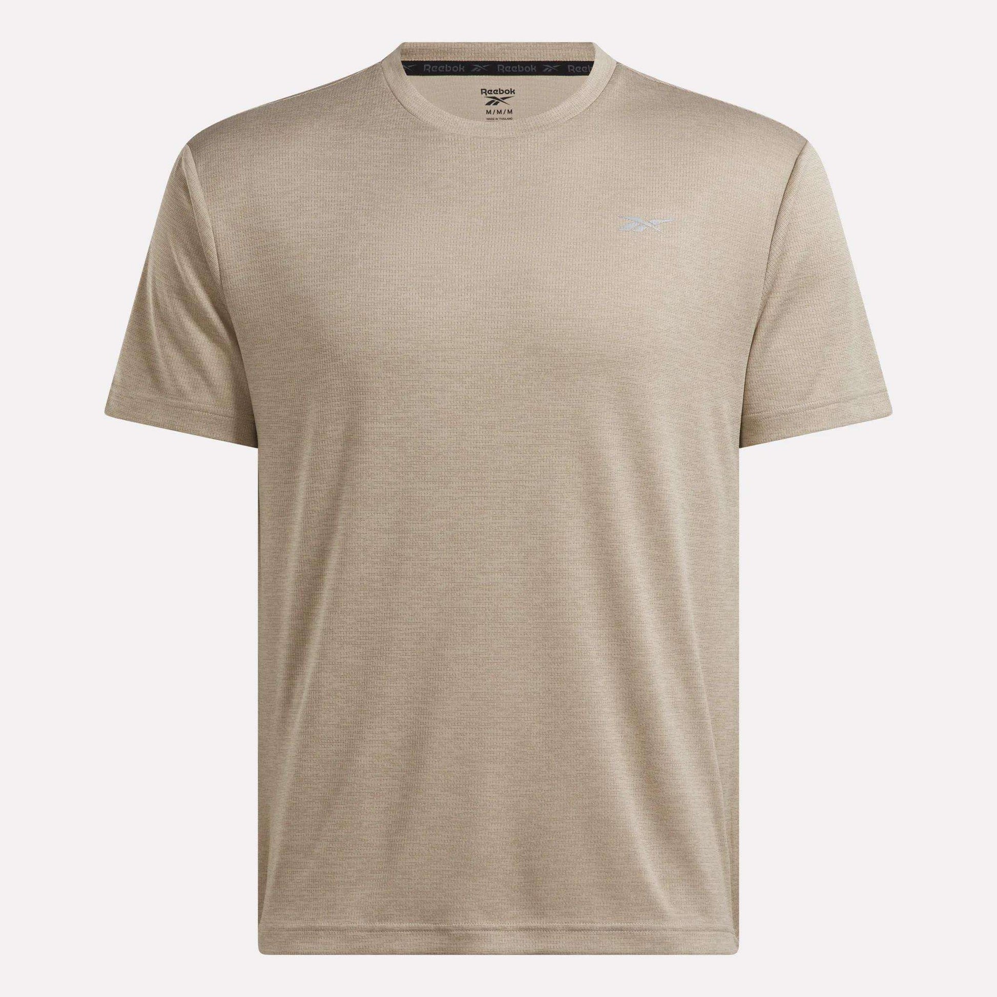 Men’s Director Short Sleeve Top by Reebok, featuring a beige color, crew neck, and short sleeves. This stretchy men’s workout shirt includes a subtle Reebok logo on the left chest and is showcased against a plain white background.
