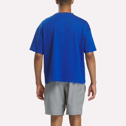 A person stands facing away against a plain white background, wearing a blue Reebok x F45 Training Graphic T-Shirt and light gray shorts.