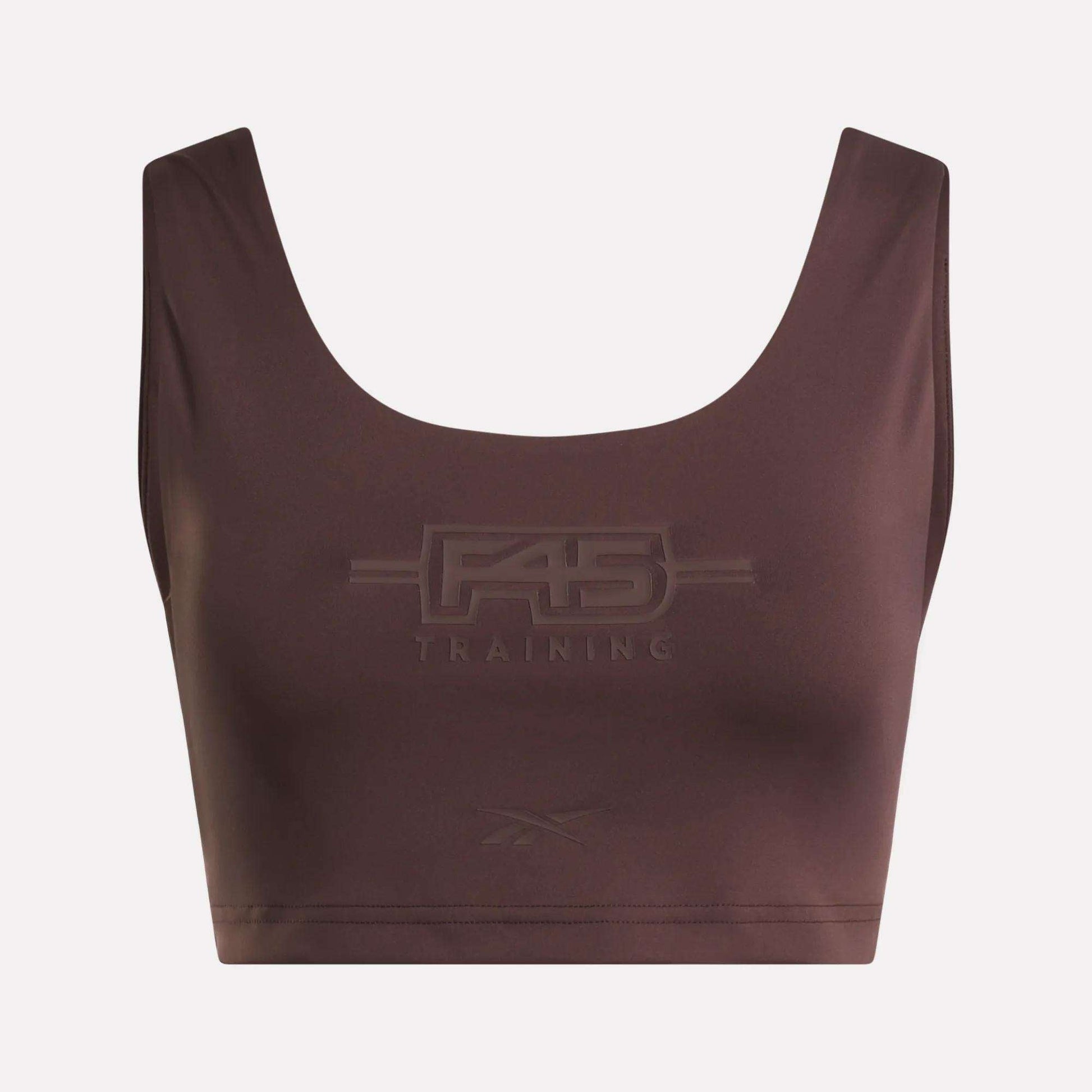 Introducing the Women's Reebok x F45 Training Sports Bra. This brown sports bra by Reebok features "F45 Training" embossed on the front, with a subtle Reebok logo beneath. Designed with a scoop neckline and wide shoulder straps, it stands out against a plain background to keep the focus on the garment.