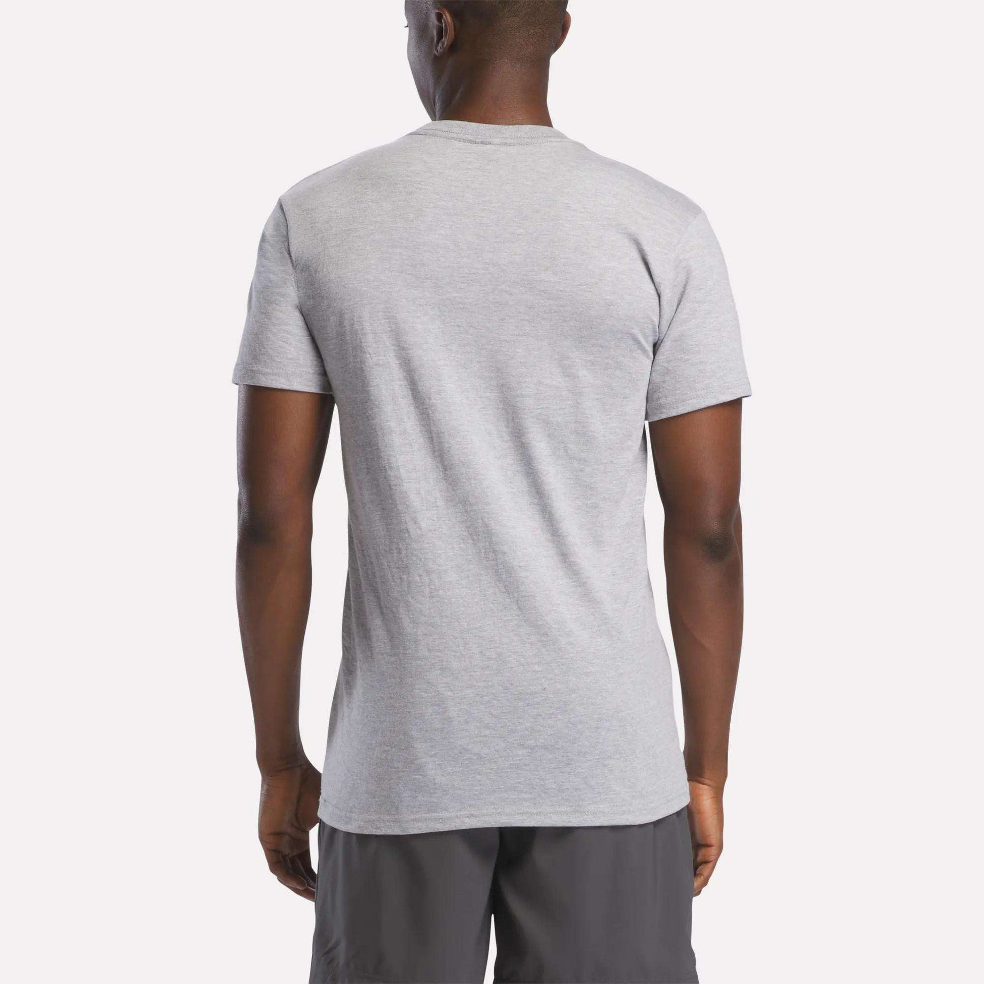 A man, back to the camera, wears a light gray Reebok Men's Stacked Vector Graphic T-Shirt made from lightweight 100% cotton with dark gray shorts, set against a plain light background.
