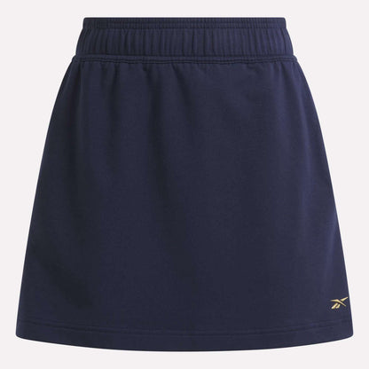 The Women's Logo Skirt by Reebok is a navy blue sports skirt with an elastic waistband, a small yellow logo near the right hem, and is made from a comfortable cotton blend.