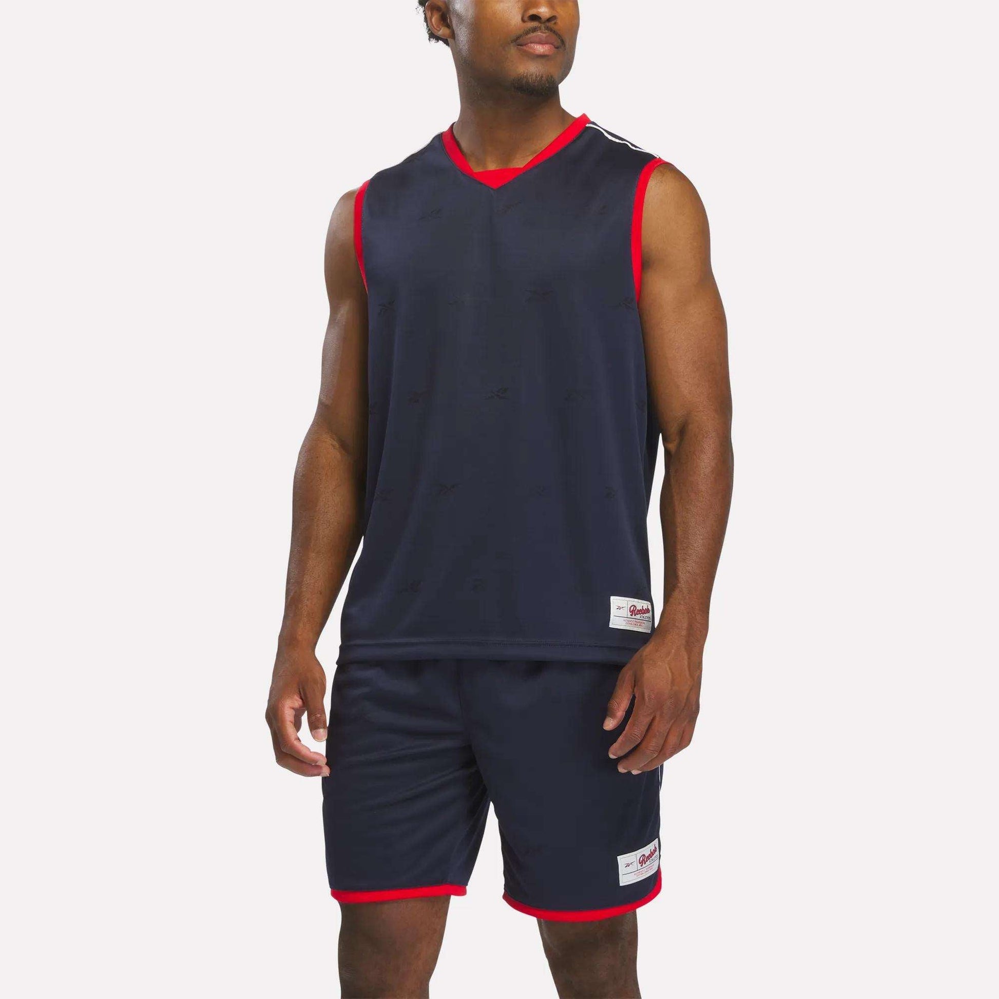 A man wears the Reebok Men's United Jersey Tank in Vector Navy, standing against a plain white background.