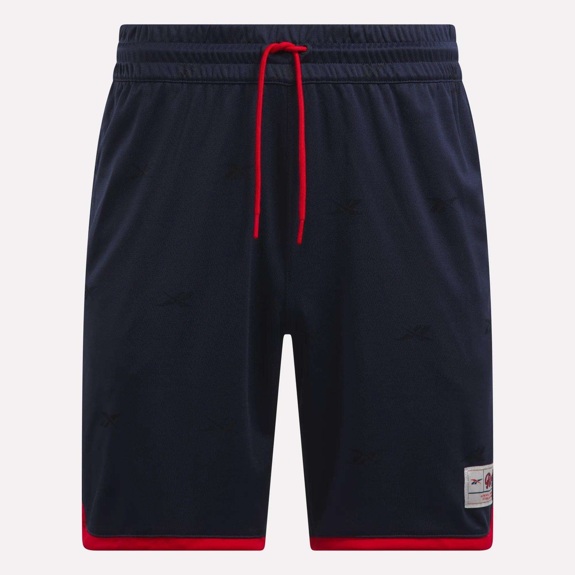 The Reebok Men's United Shorts 9" are navy blue lightweight polyester shorts with red trim at the leg openings, a red drawstring, subtle logo patterns, and a small logo patch near the left hem.