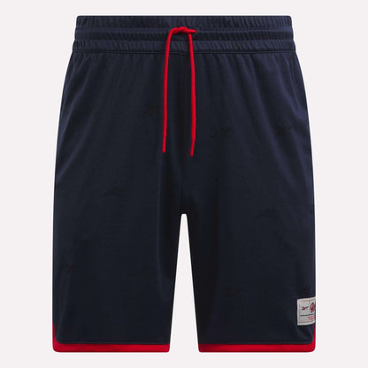 The Reebok Men's United Shorts 9" are navy blue lightweight polyester shorts with red trim at the leg openings, a red drawstring, subtle logo patterns, and a small logo patch near the left hem.