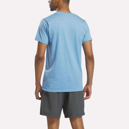 A person stands with their back to the camera, wearing a Reebok Men's Stacked Vector Graphic T-Shirt in light blue and dark gray shorts, set against a plain light background.