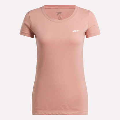 The Reebok Women's T-Shirt features a plain light pink cotton design with short sleeves, a round neckline, and a small white Reebok logo on the left chest, shown against a white background.