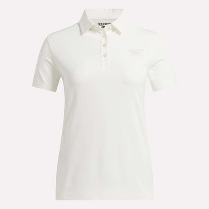 The Reebok Women's Solid Core Polo Shirt is a white, short-sleeve golf top featuring a classic collar and button placket. Made from performance jersey for comfort and breathability, it displays a subtle Reebok logo on the left chest. The shirt is shown against a plain white background.