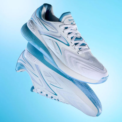A pair of Reebok Nano X5 Edge Training Shoes in white and light blue are shown against a gradient blue background, with one shoe above its reflection, showcasing their sleek design and Flexweave-textured sole.