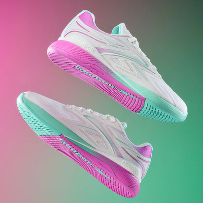 Two white Reebok Women's Nano X5 Edge Training Shoes with pastel pink, purple, and mint green accents float against a pink and green gradient backdrop, highlighting their colorful soles and sleek Reebok design.