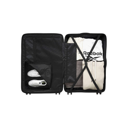 An open suitcase neatly packed with folded clothes and a pair of white sneakers in a separate compartment. The clothes are secured with crossed straps, including a white t-shirt with a visible Reebok logo.