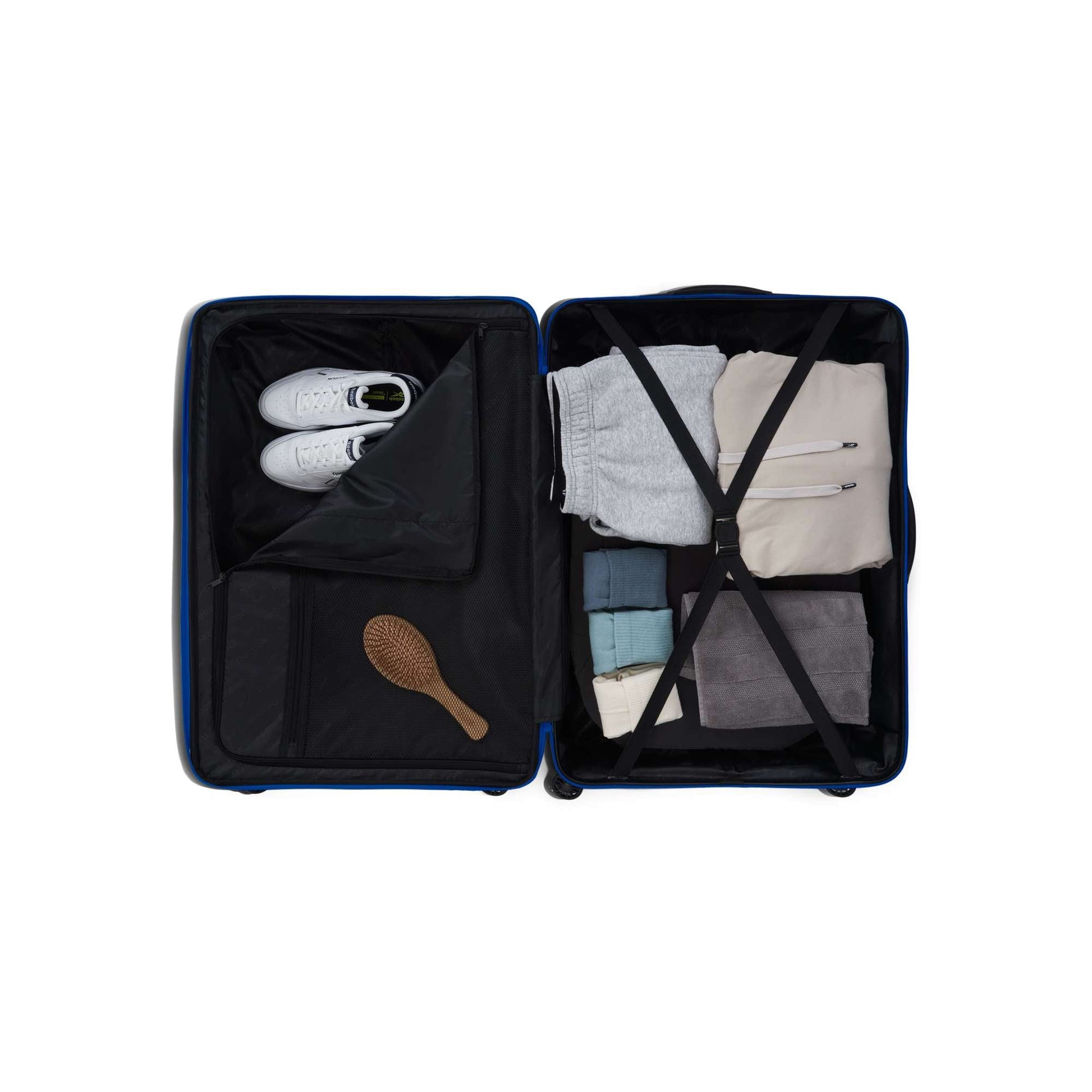 An open Reebok Action Duo 2 Piece Luggage Set displays neatly folded clothes, a pair of white sneakers, a brown hairbrush, and clothing items secured with interior straps.