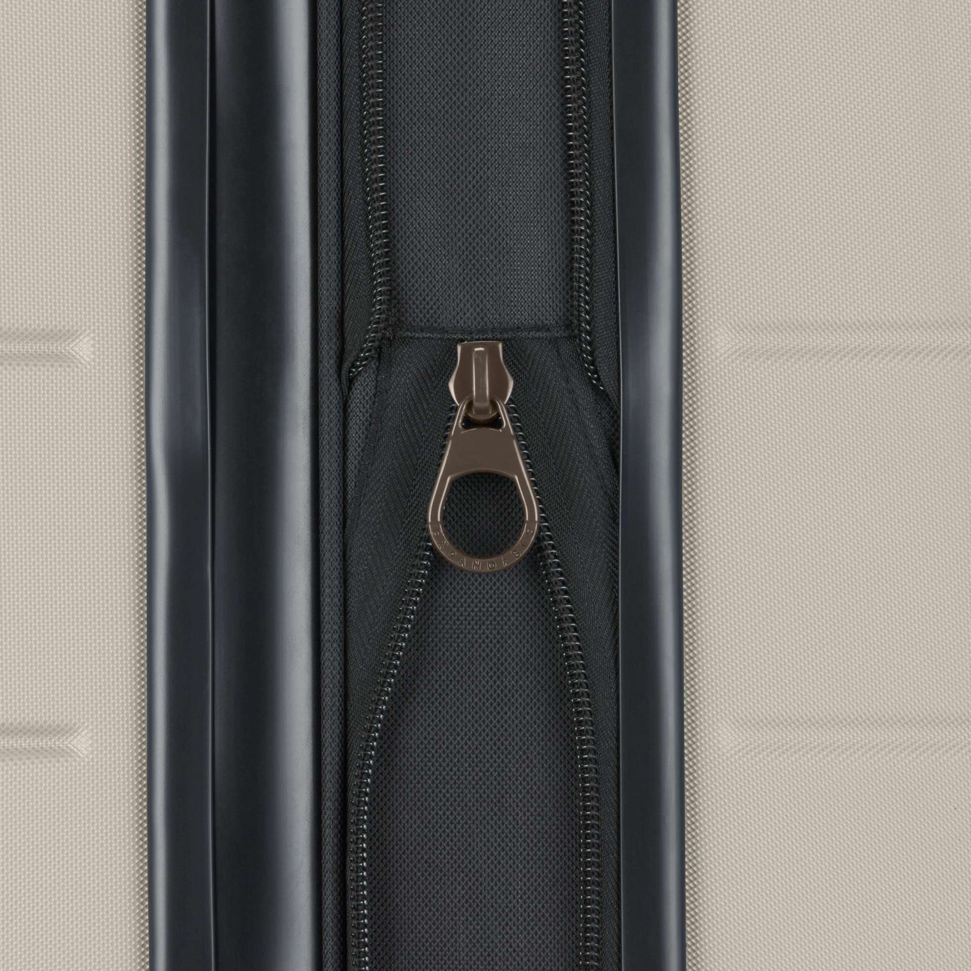 Close-up of a metallic zipper pull on a black zipper against a textured light beige background, featured on the Reebok Captain 2 Piece Luggage Set—a durable choice for travelers.