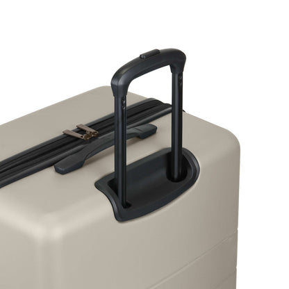 A close-up of a beige hard-shell suitcase with a black telescopic handle extended and a black zipper along the top.