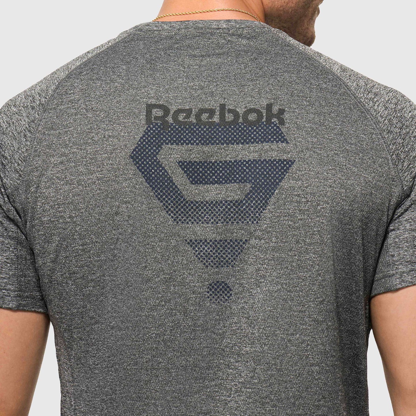 A person is shown from the back wearing a lightweight Reebok x GLDN PNT Tech Tee in heather gray, featuring a large dark Reebok logo and graphic design across the upper back.