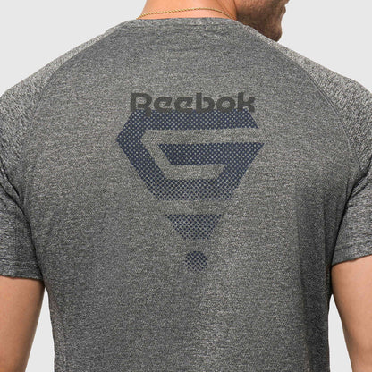 A person is shown from the back wearing a lightweight Reebok x GLDN PNT Tech Tee in heather gray, featuring a large dark Reebok logo and graphic design across the upper back.