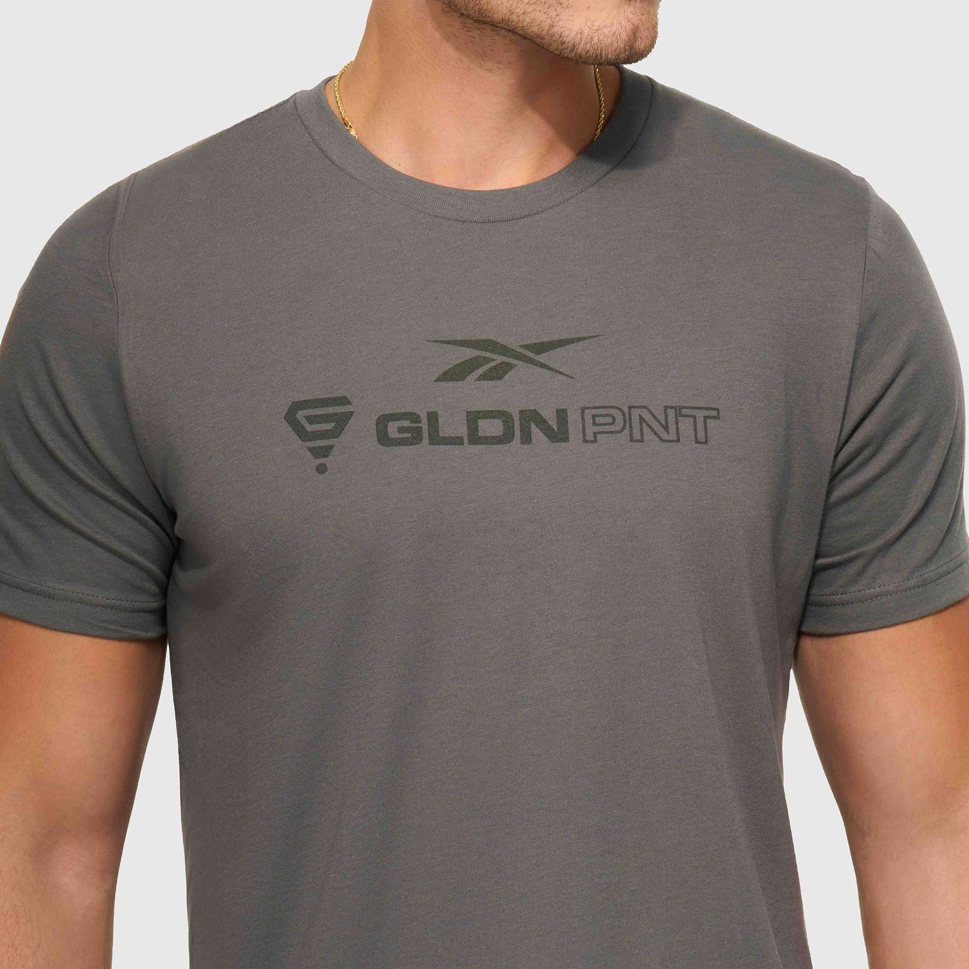 A person models the Reebok x GLDN PNT Jersey Tee, featuring “GLDN PNT” and two logos on the chest, shown from shoulders to waist against a plain background.
