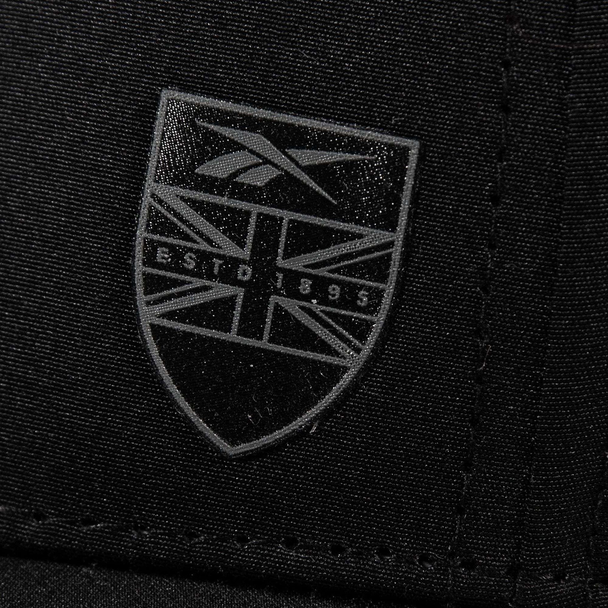 Close-up of black Chip Pro fabric by Reebok, showcasing a shield-shaped logo with the Union Jack pattern and gray "ESTD 1895" text.