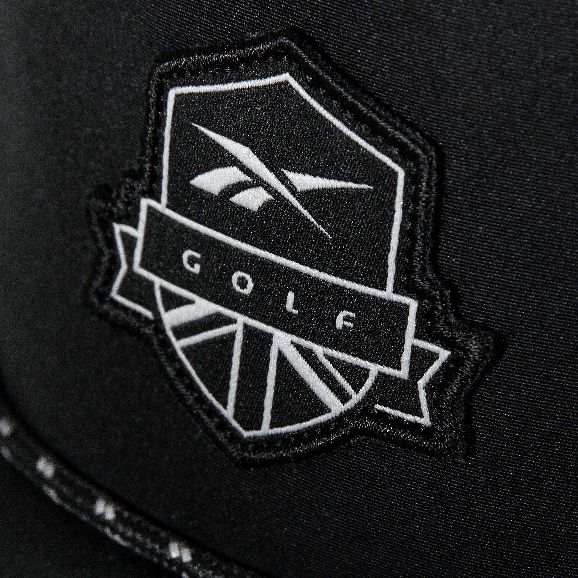 A close-up of the Madison Ii by Reebok shows a black patch with a white shield and stylized logo reading "GOLF" in bold, featured on a recycled polyester hat with an adjustable snapback.
