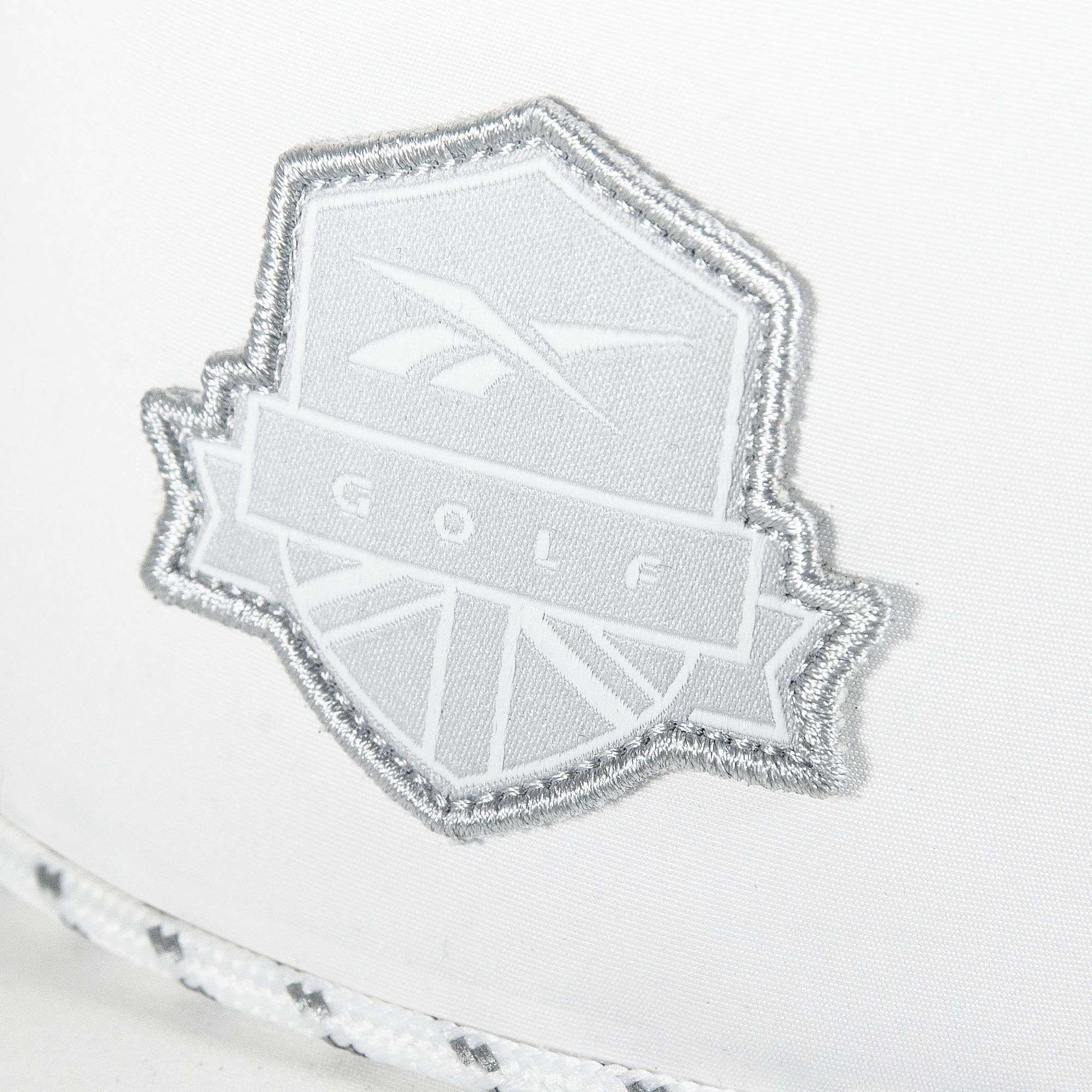 A close-up of the Reebok Madison Ii white embroidered patch, featuring GOLF and an abstract logo on recycled polyester fabric, accented with braided white and gray trim below.