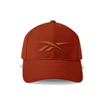 The Vector Baseball Cap by Reebok features a rust-red design, curved brim, adjustable snapback closure, and a matching rust-red embroidered Reebok logo on the front.