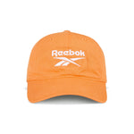 The Reebok Logo Cap features bright orange cotton twill, a curved brim, and a white embroidered logo on the front. It has an adjustable buckle closure for a custom fit and is shown against a white background.