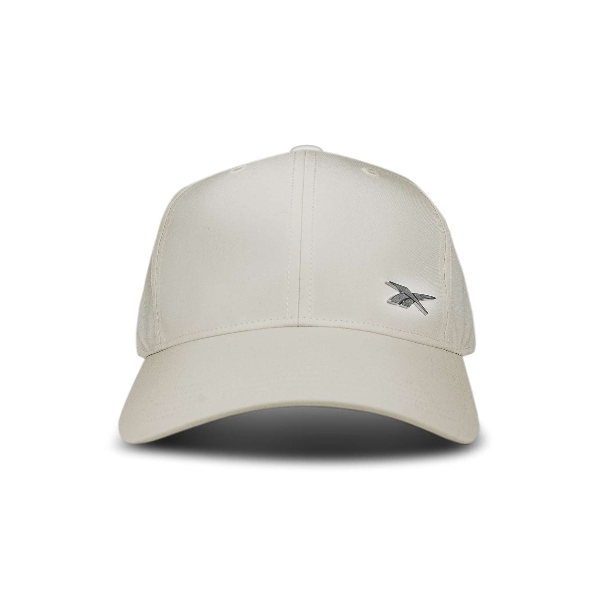 The Reebok Badge Cap is a beige baseball cap featuring a small silver embroidered logo on the front left side, shown against a white background.