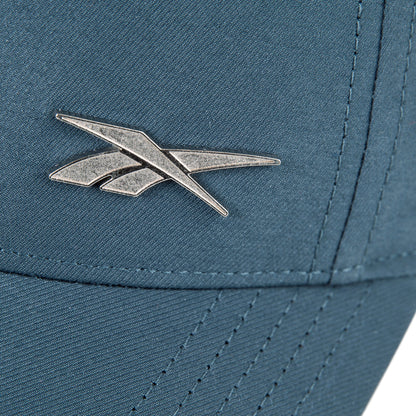 Close-up of the Reebok Badge Cap in teal, showing a silver metallic logo on the front and visible stitching on the moisture-wicking fabric.